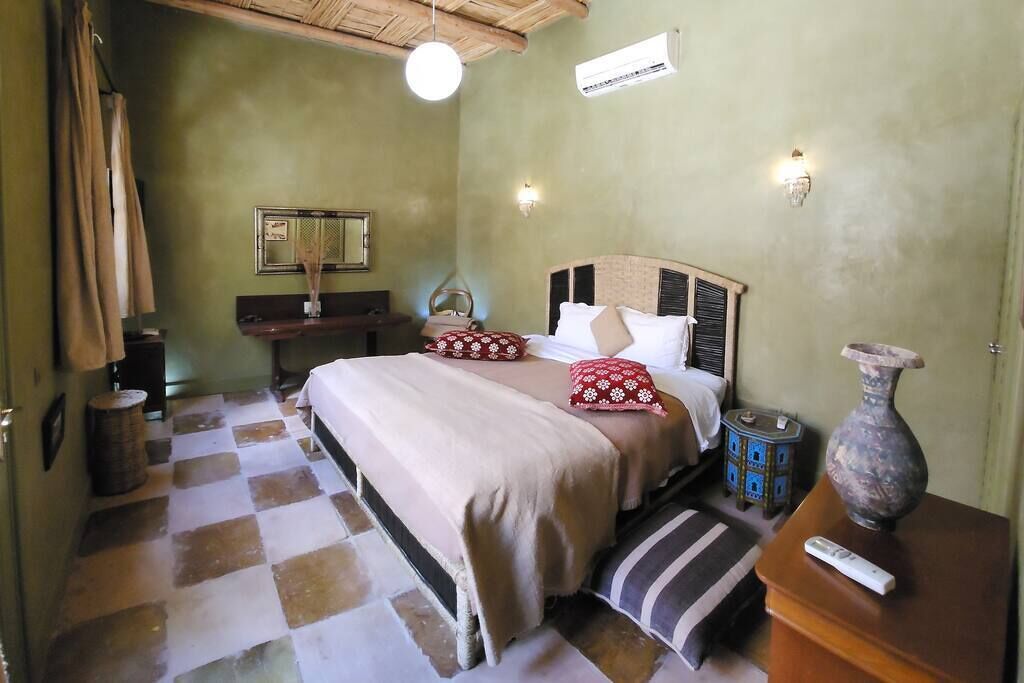 Une chambre à coucher comprenant un lit, une table de chevet, une lampe, un miroir et un petit vase décoratif.