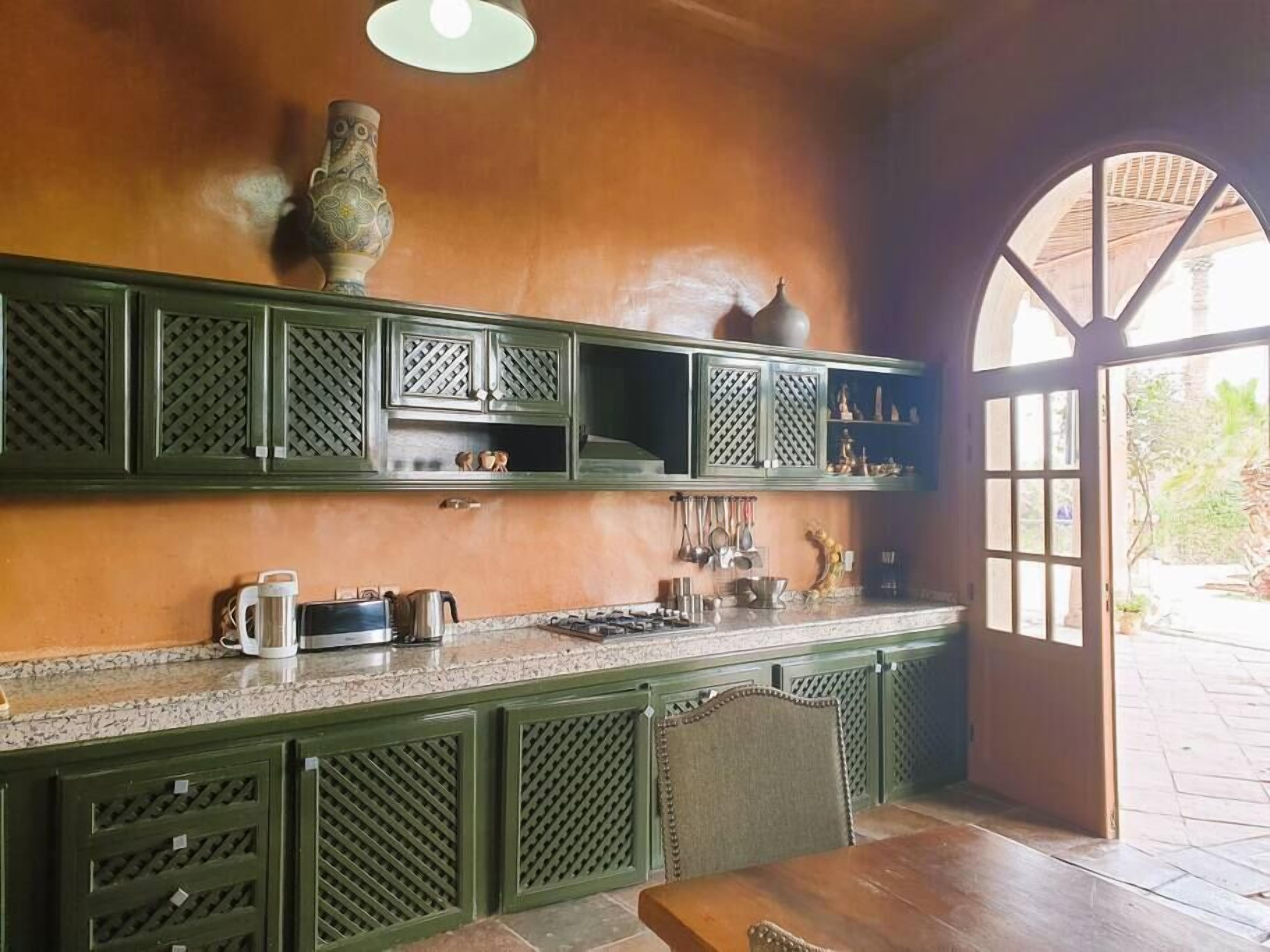 A kitchen with green cabinetry, a gas stove, and a dining area with a table and chairs.