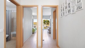 Un couloir comprenant une douche, des toilettes et un lit recouvert d’une couverture verte. Des tableaux encadrés ornent le mur.