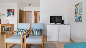 Une pièce avec deux chaises, un téléviseur posé sur un meuble, une bibliothèque et un tableau accroché au mur.