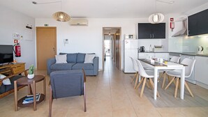A modern apartment with a living room, dining area, kitchenette, and a hallway leading to another room.