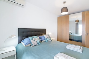 A bedroom with a bed, a nightstand, a lamp, a wardrobe, and a mirror.