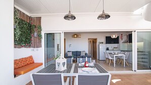 A modern dining area with a table set for two, a sofa, and a kitchen in the background.