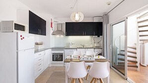 A modern kitchen with white cabinets, a built-in oven, a microwave, and a dining area with two chairs and a table.