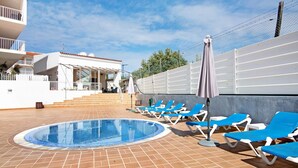 A swimming pool with blue lounge chairs and a white building with a balcony.