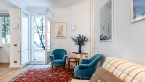 A living room with a red patterned rug, two blue armchairs, a beige sofa, and a small table with a vase of flowers. - Almond Blossom, by Veeve (Paris)
