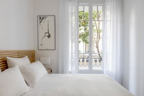 A hotel room with a bed, a nightstand, a lamp, a framed artwork, and a view of a balcony with greenery. - Almond Blossom, by Veeve (Paris)