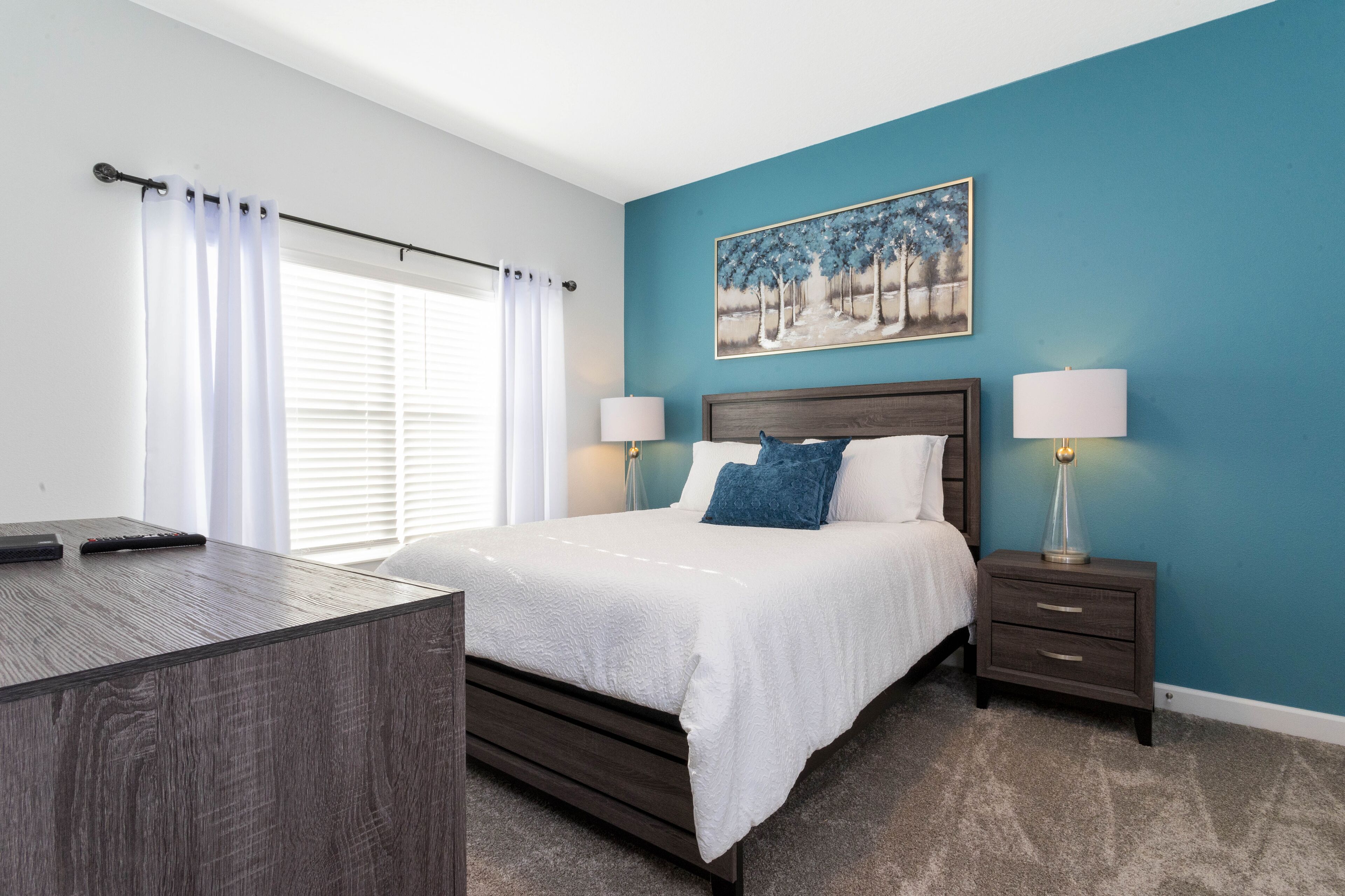 A bedroom with a bed, bedside tables, a desk, and a painting on the wall.