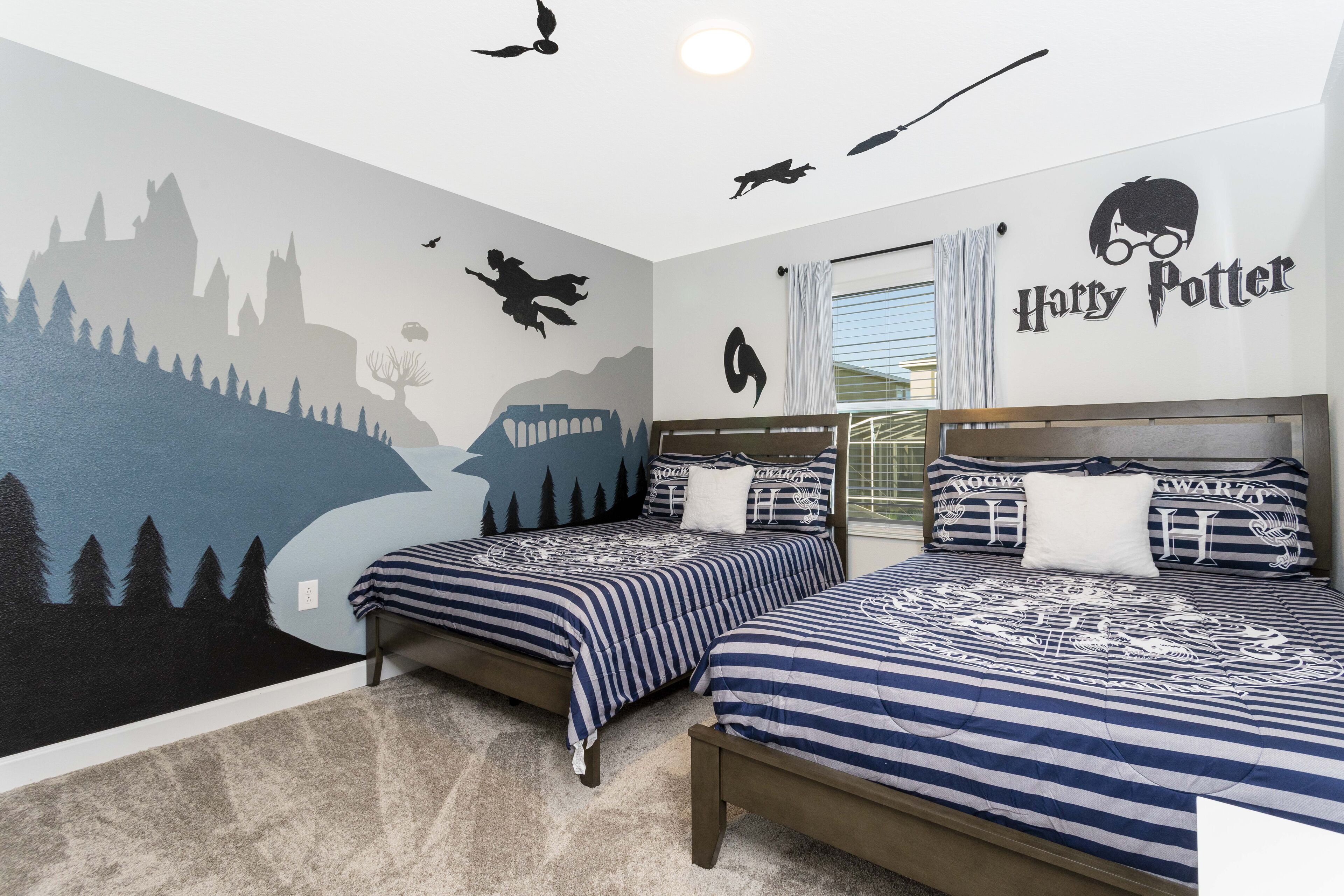 A bedroom with two beds, a mural of a landscape, and a Harry Potter logo on the wall.