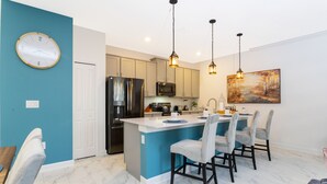 Una cocina moderna con una isla central, iluminación colgante y un comedor con taburetes de bar.