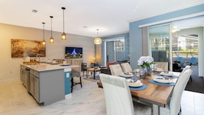 Una cocina moderna con una isla central, comedor con una mesa y sillas de madera, y un ventanal con vistas al exterior.