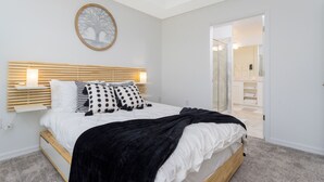 A bedroom with a bed, bedside tables, a wall-mounted tree decoration, and a bathroom visible through an open door. - Gorgeous 3Bd 8 Guests @Storey Lake Resort Close to Disney 101 3191 (Kissimmee)
