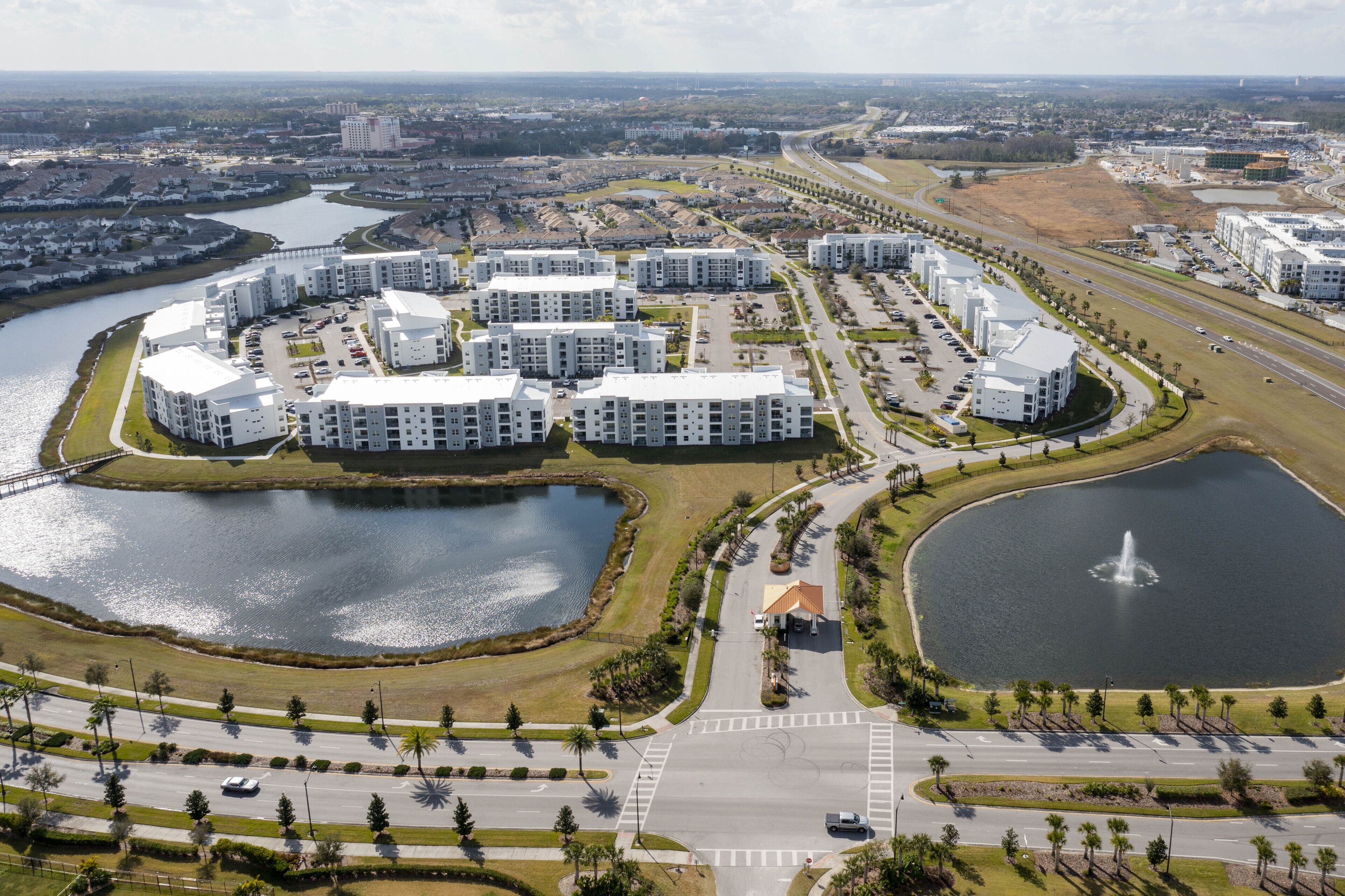 A modern residential complex with multiple apartment buildings, a central road, and surrounding water bodies.