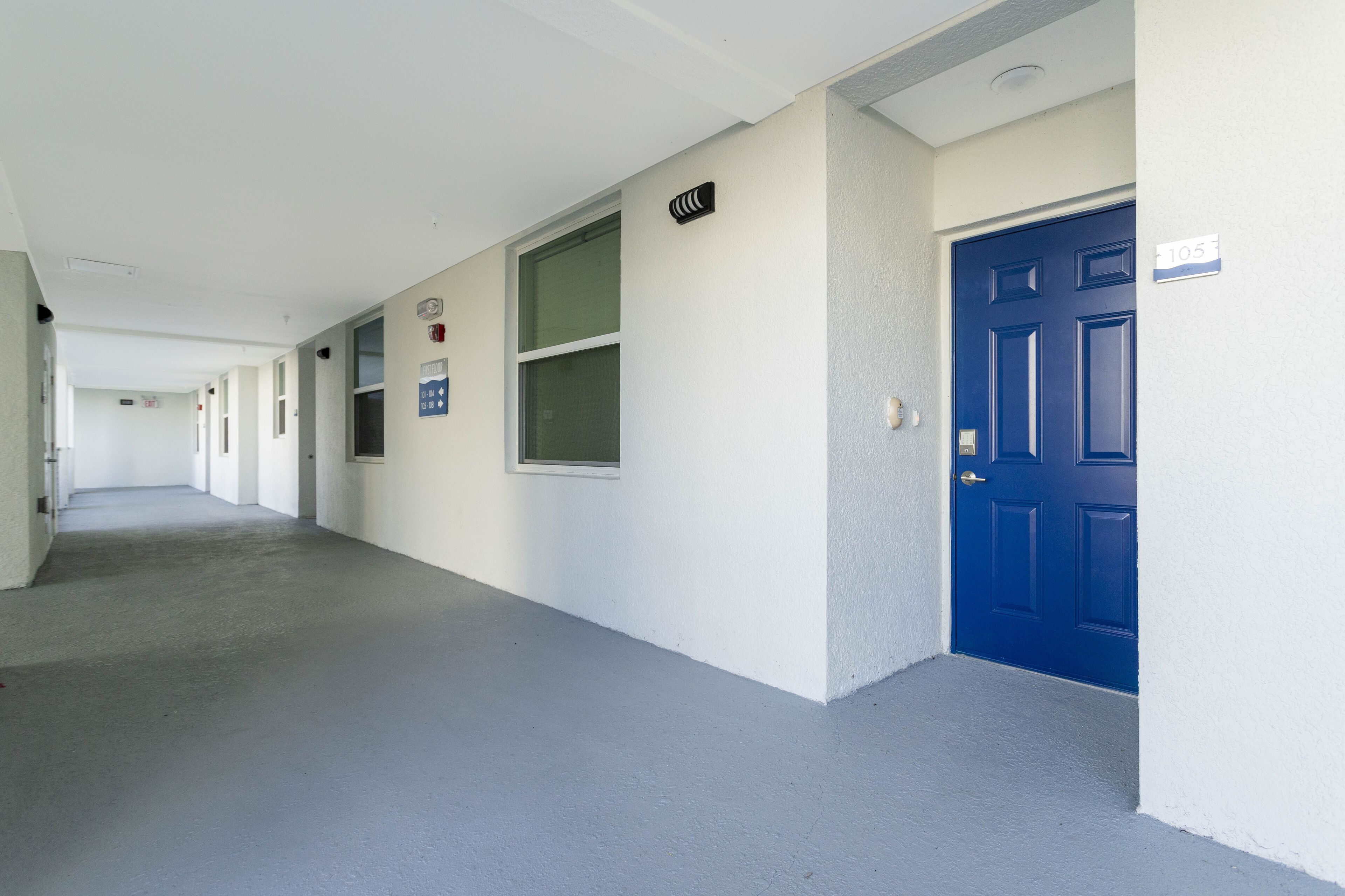 A long, narrow hallway with white walls and a blue door on the right.