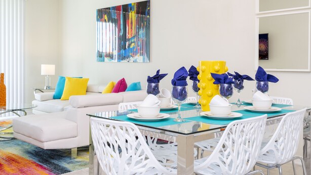 A modern dining area with a glass table, white chairs, and colorful cushions on a white sofa. - Family Friendly 2 Bd Close to Disney @ Storey Lake 105 3161 (Kissimmee)