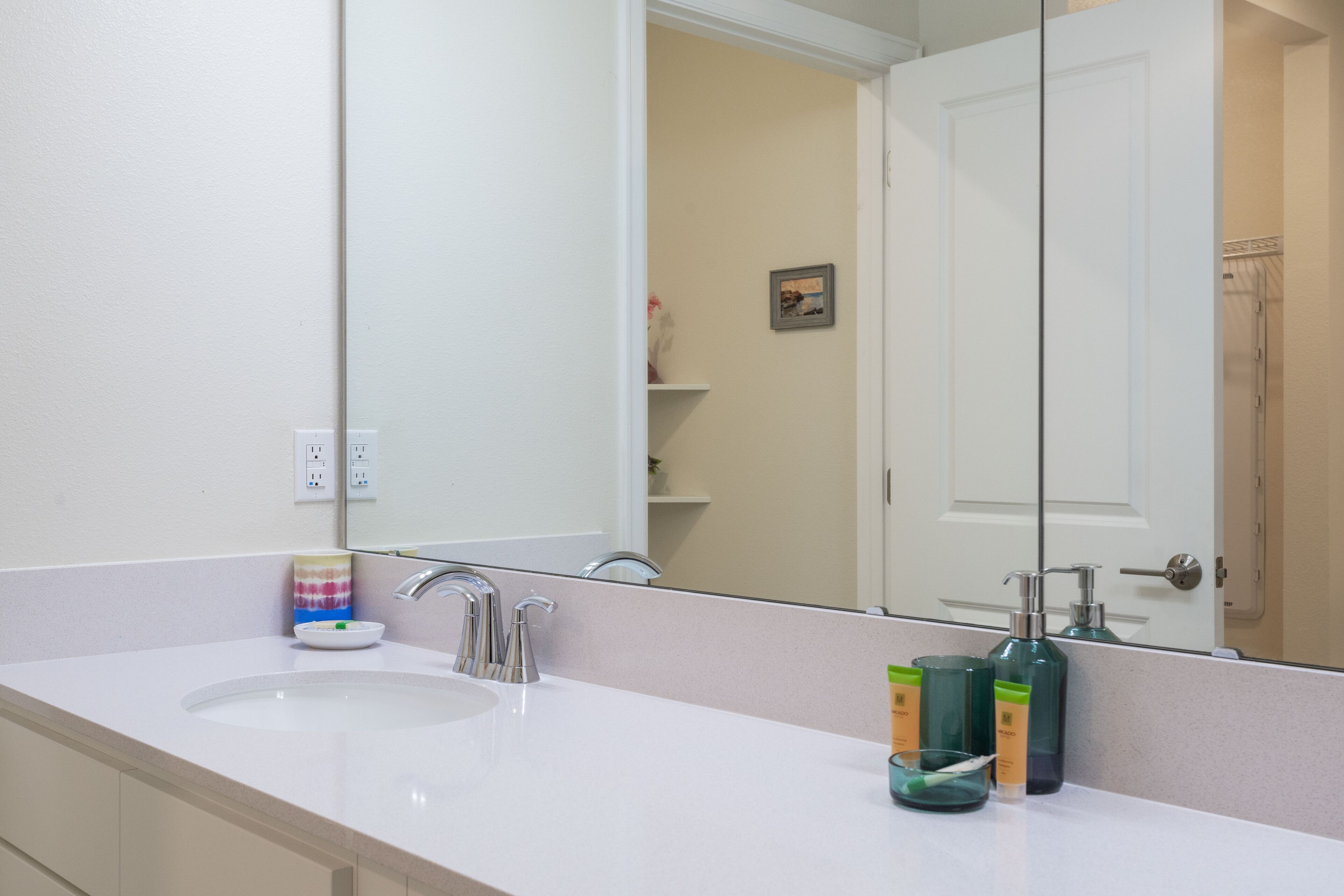 Un baño con lavamanos blanco, un espejo y artículos de aseo en la encimera.