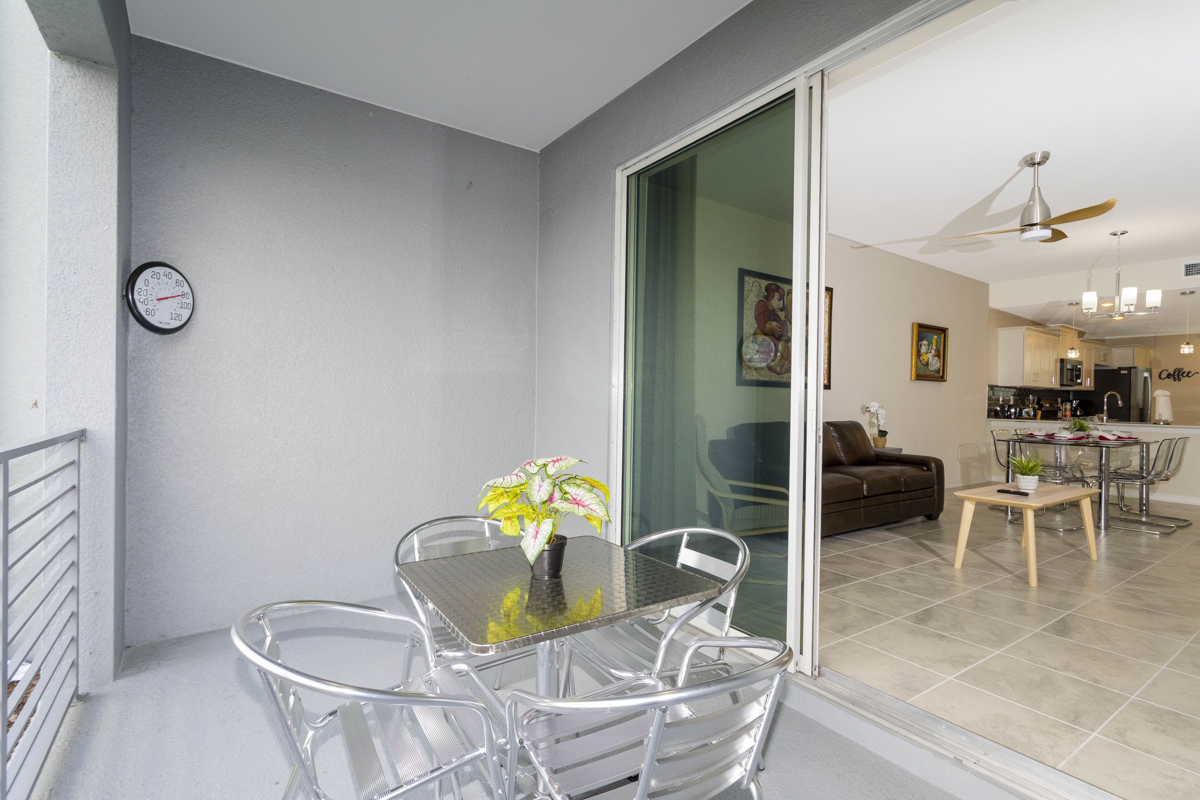 A balcony with a glass table and chairs, a potted plant, and a wall clock.