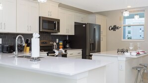 A modern kitchen with white cabinetry, stainless steel appliances, and a bar area with stools. - Stunning 2Bd Apto Close to Disney @ Storey Lake 105 3171 (Kissimmee)