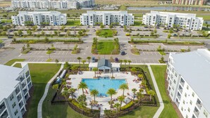 An aerial view of a modern hotel complex with multiple buildings, a central swimming pool, and landscaped areas. - Stunning 2Bd Apto Close to Disney @ Storey Lake 105 3171 (Kissimmee)