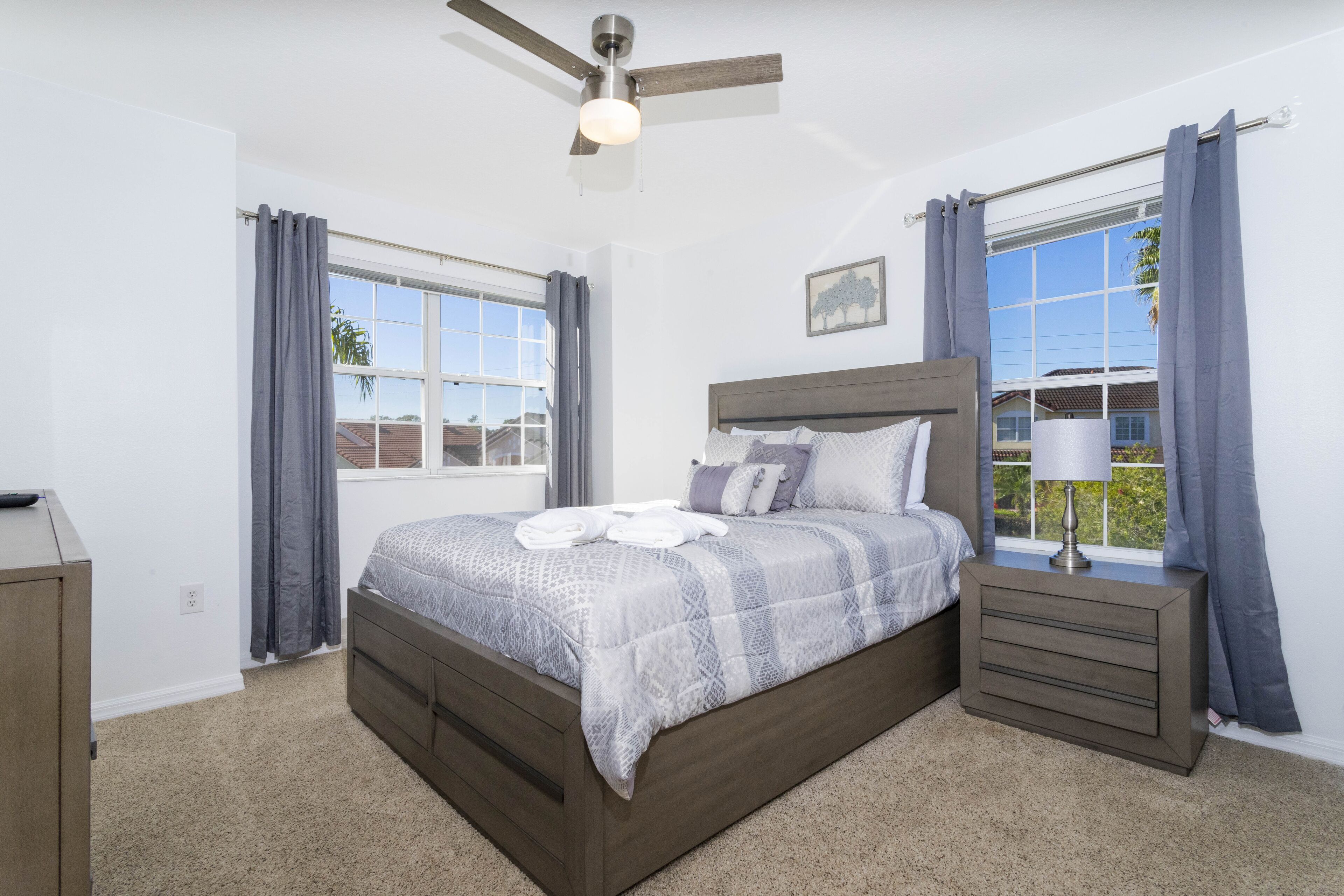 A bedroom with a bed, bedside tables, a ceiling fan, and a window with curtains.