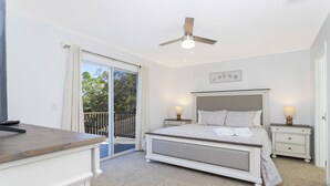 Un dormitorio con cama, mesitas de noche, ventilador de techo y vista al exterior.