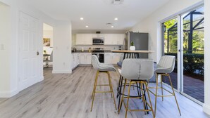 Una cocina moderna con armarios blancos, un refrigerador de acero inoxidable y una zona de comedor con taburetes de bar.
