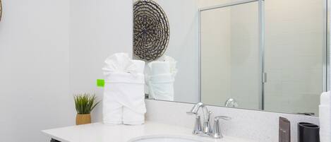 Une salle de bain moderne avec un lavabo blanc, un grand miroir et une cabine de douche.