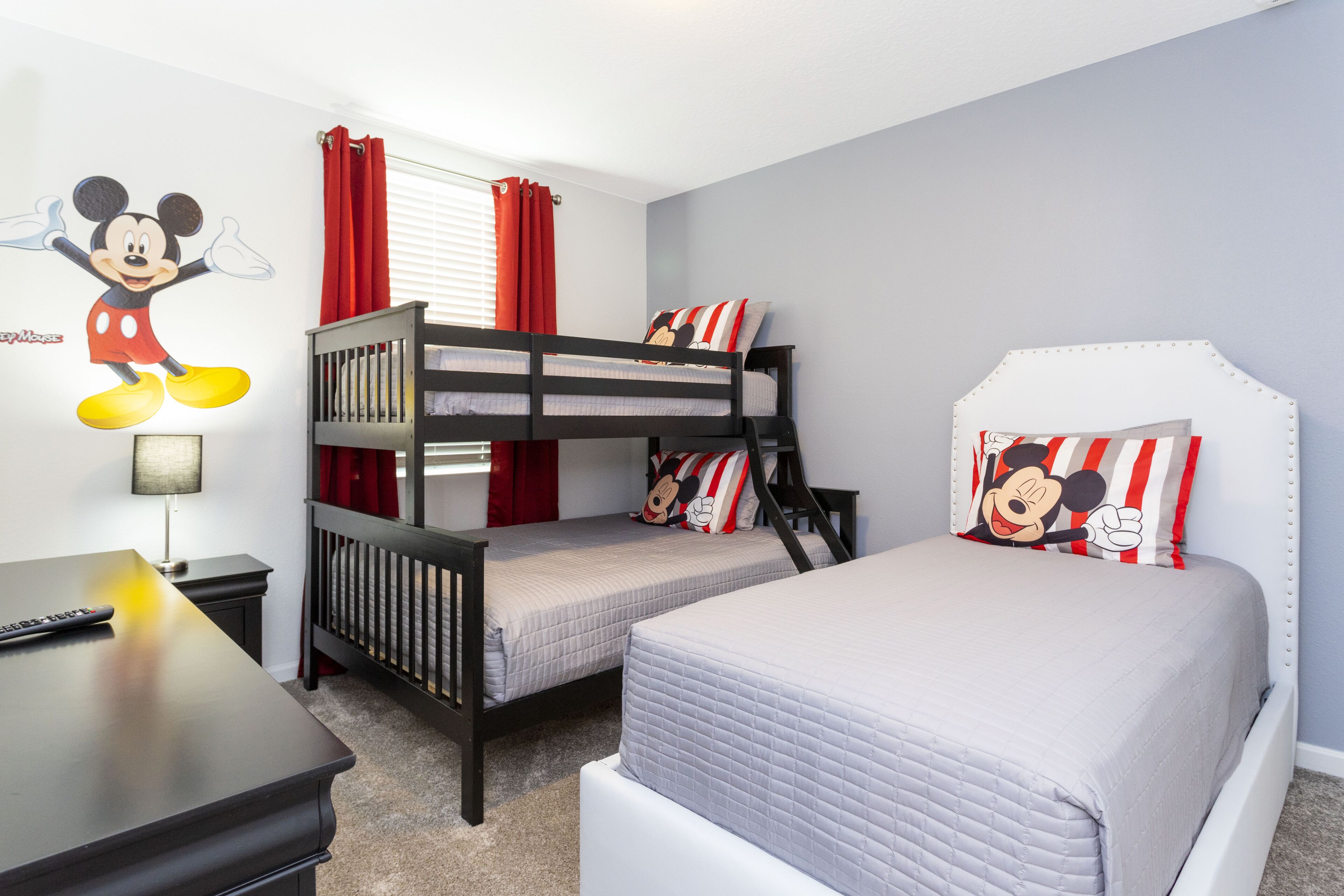A child's bedroom with bunk beds, a desk, and a Mickey Mouse wall decal.