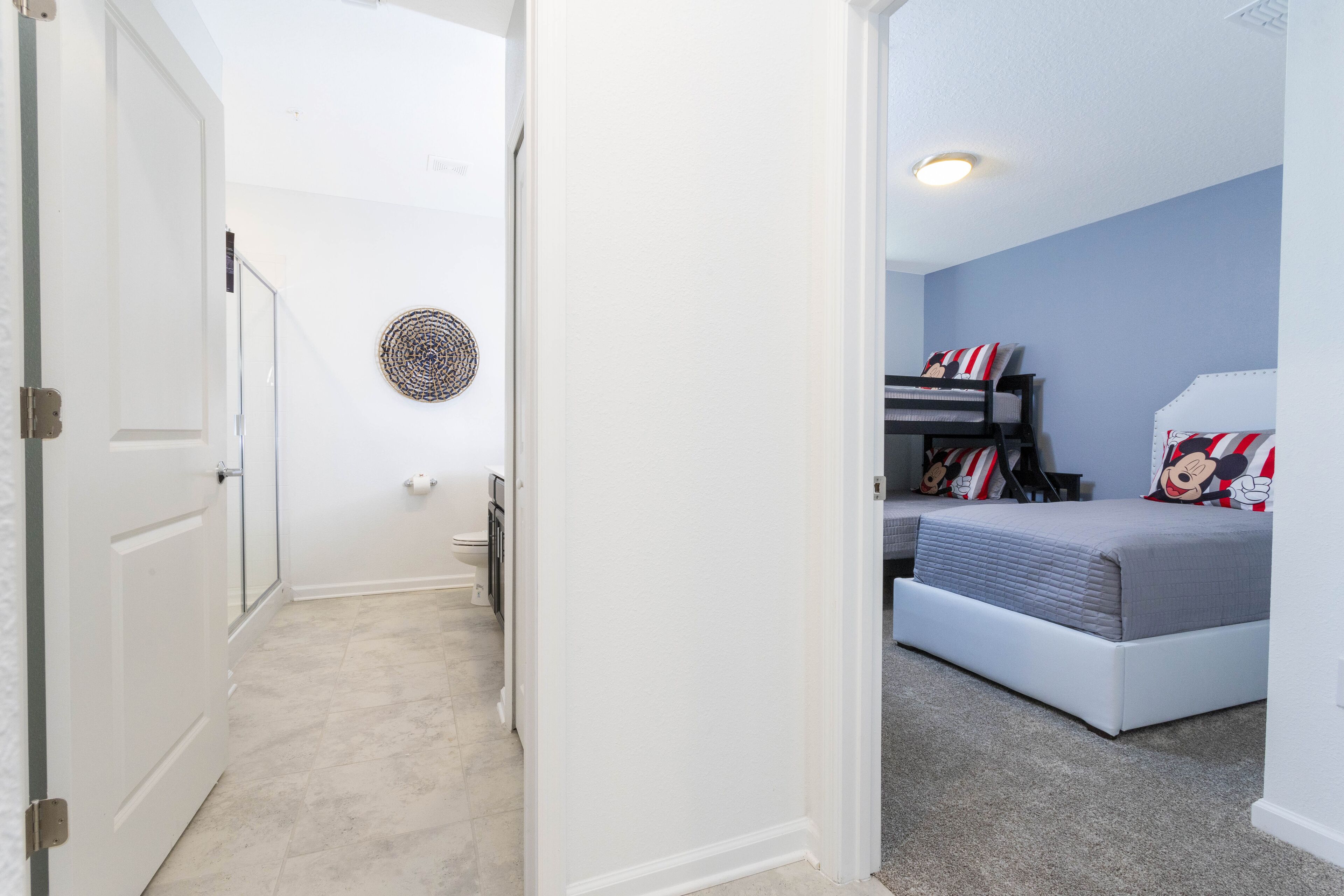 A bedroom with a bunk bed, a circular wall decoration, and a hallway leading to a bathroom.