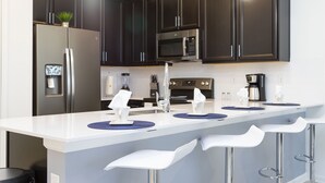 A modern kitchen with dark cabinets, a white countertop, stainless steel appliances, and bar stools.