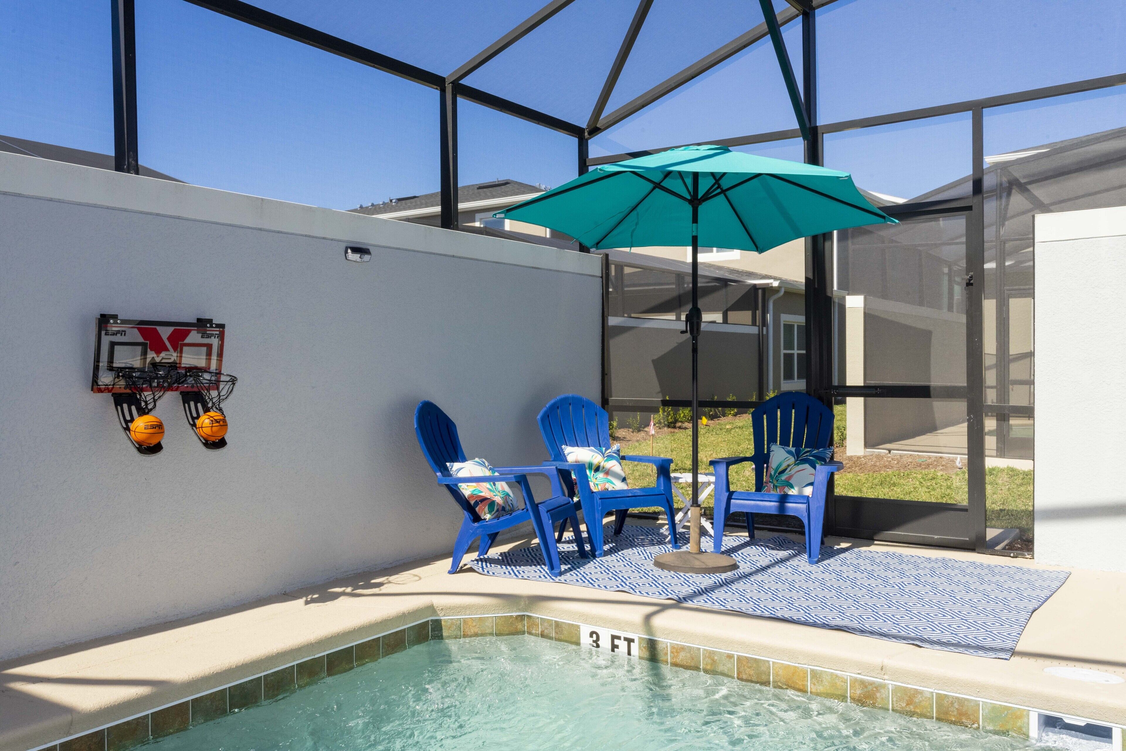A swimming pool area with two blue chairs and a green umbrella.