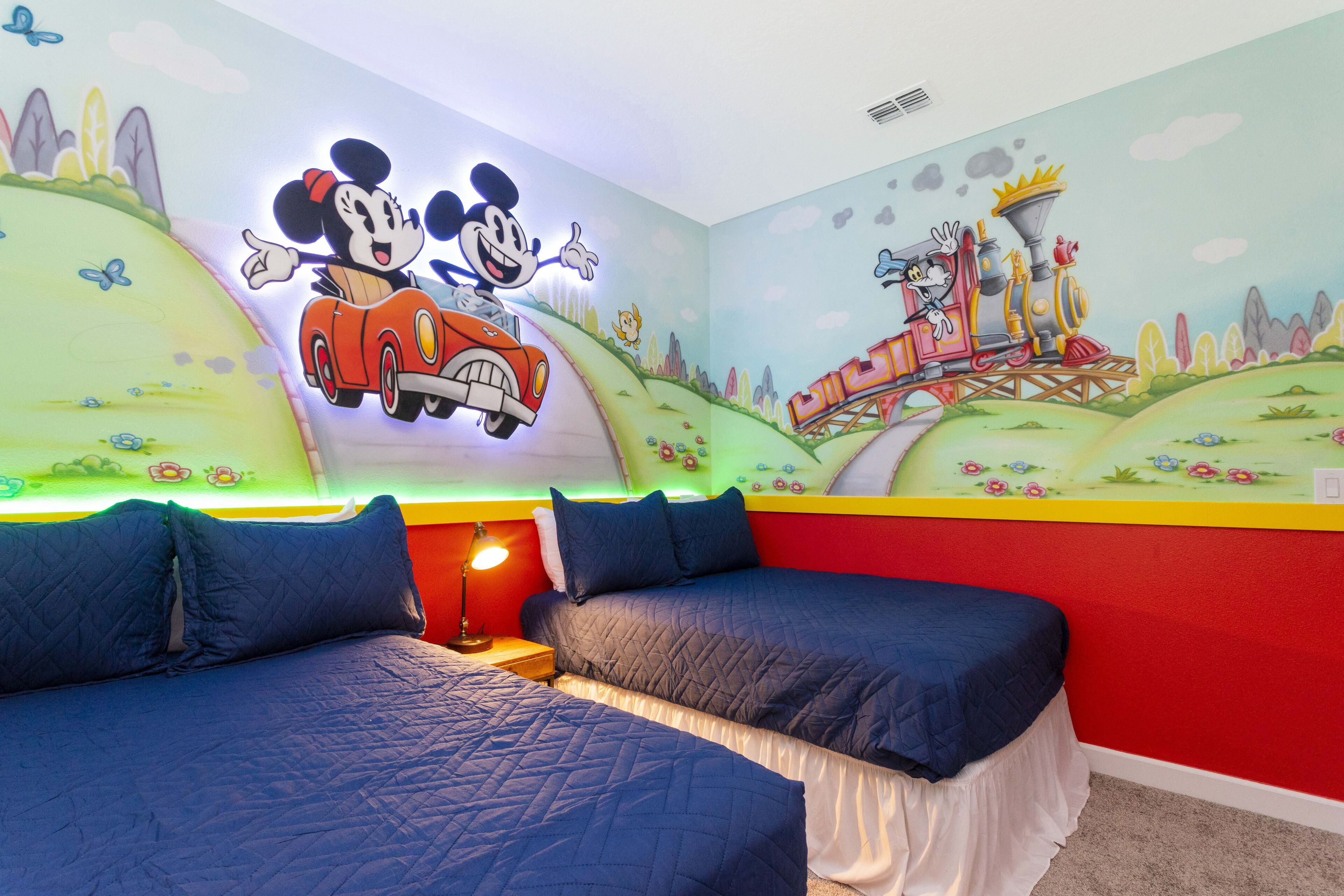 Ein Kinderzimmer mit zwei Betten, bunten Wandmalereien und einer Deckenleuchte im Mickey Mouse-Design.