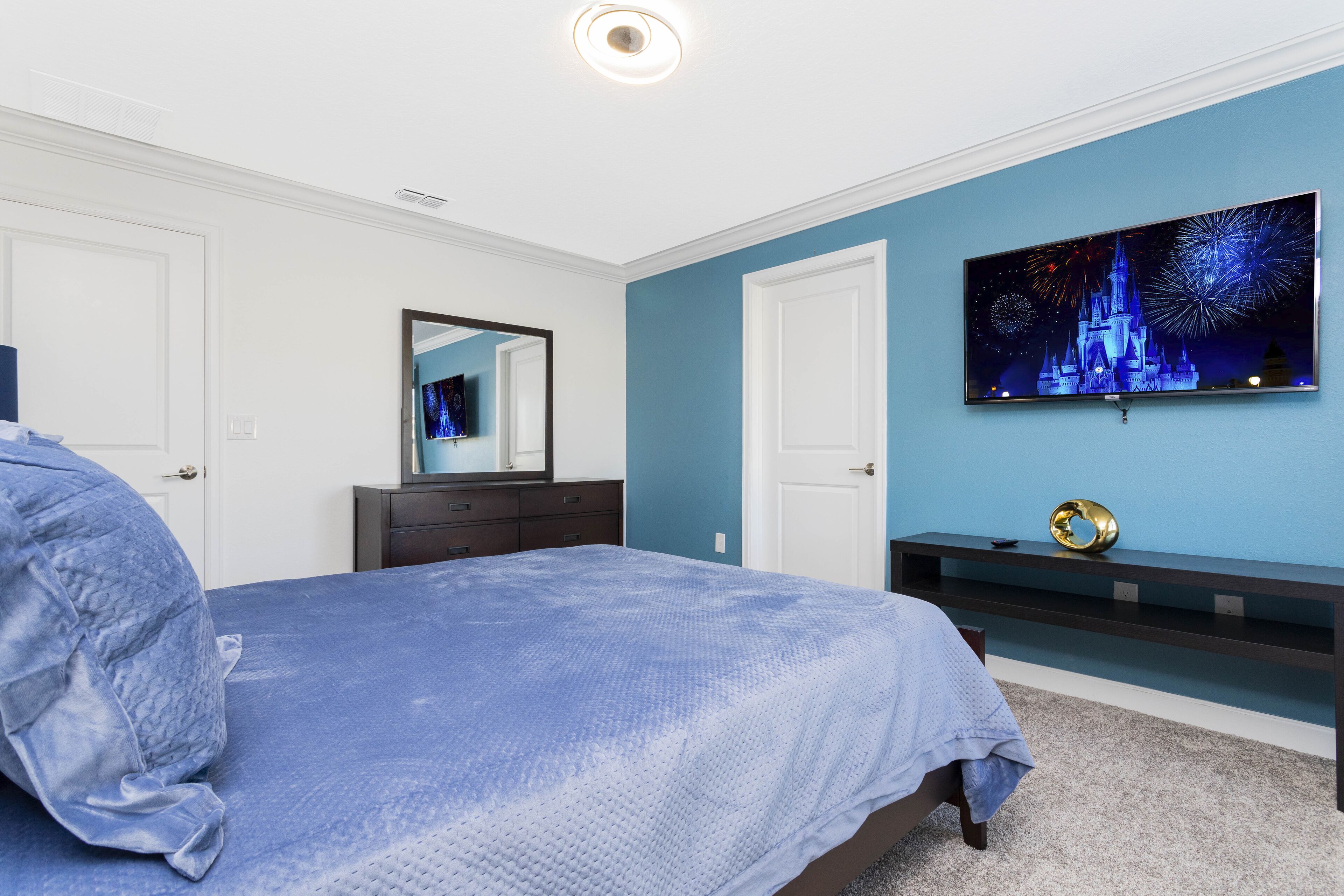 Een slaapkamer met een bed, een dressoir, een spiegel, een televisie en een kunstwerk aan de muur.
