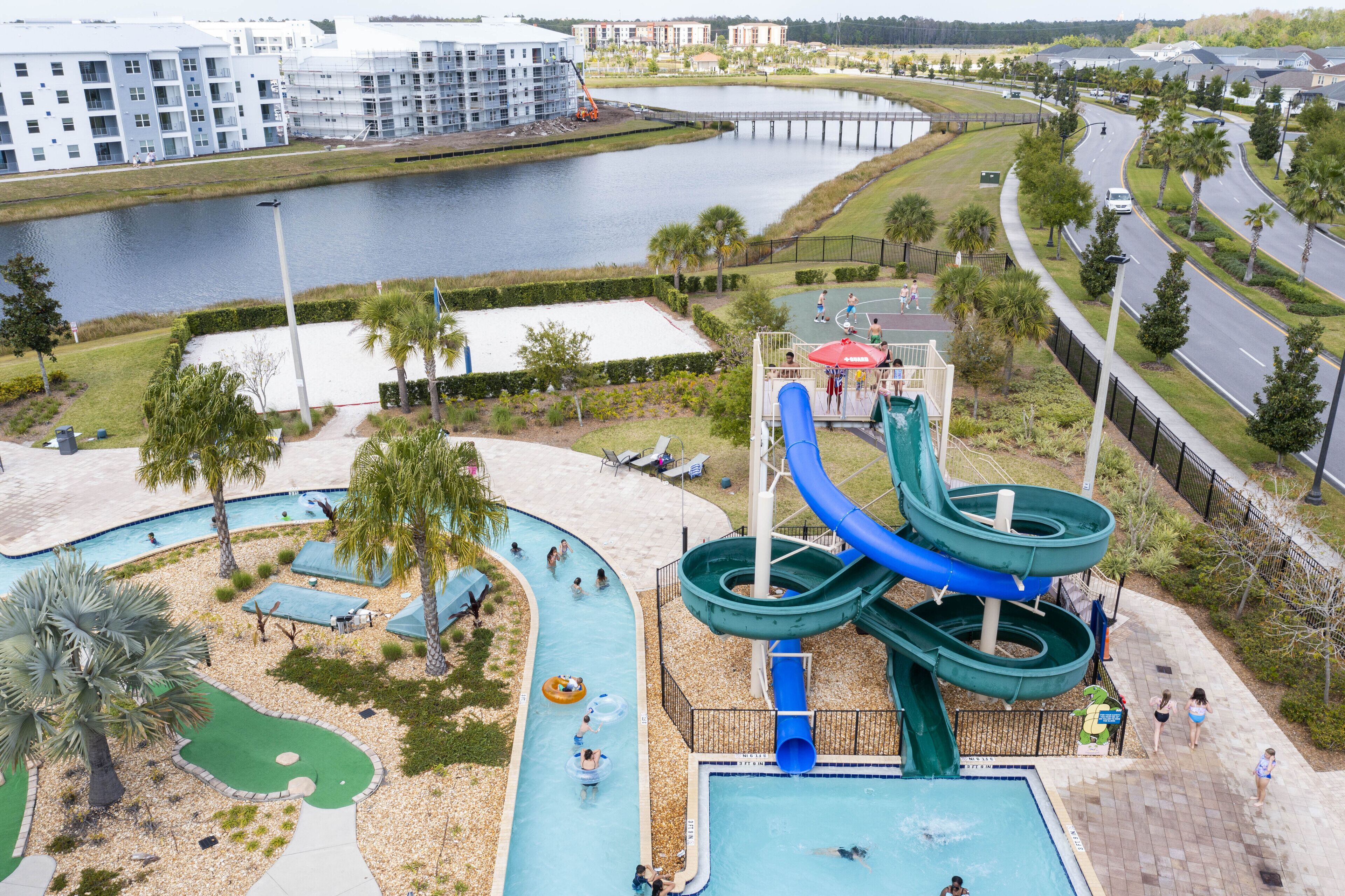 Un parc aquatique doté de nombreux toboggans et de plusieurs piscines, entouré d’un espace paysager agrémenté de palmiers, et offrant une vue sur une rivière et des bâtiments en arrière-plan.