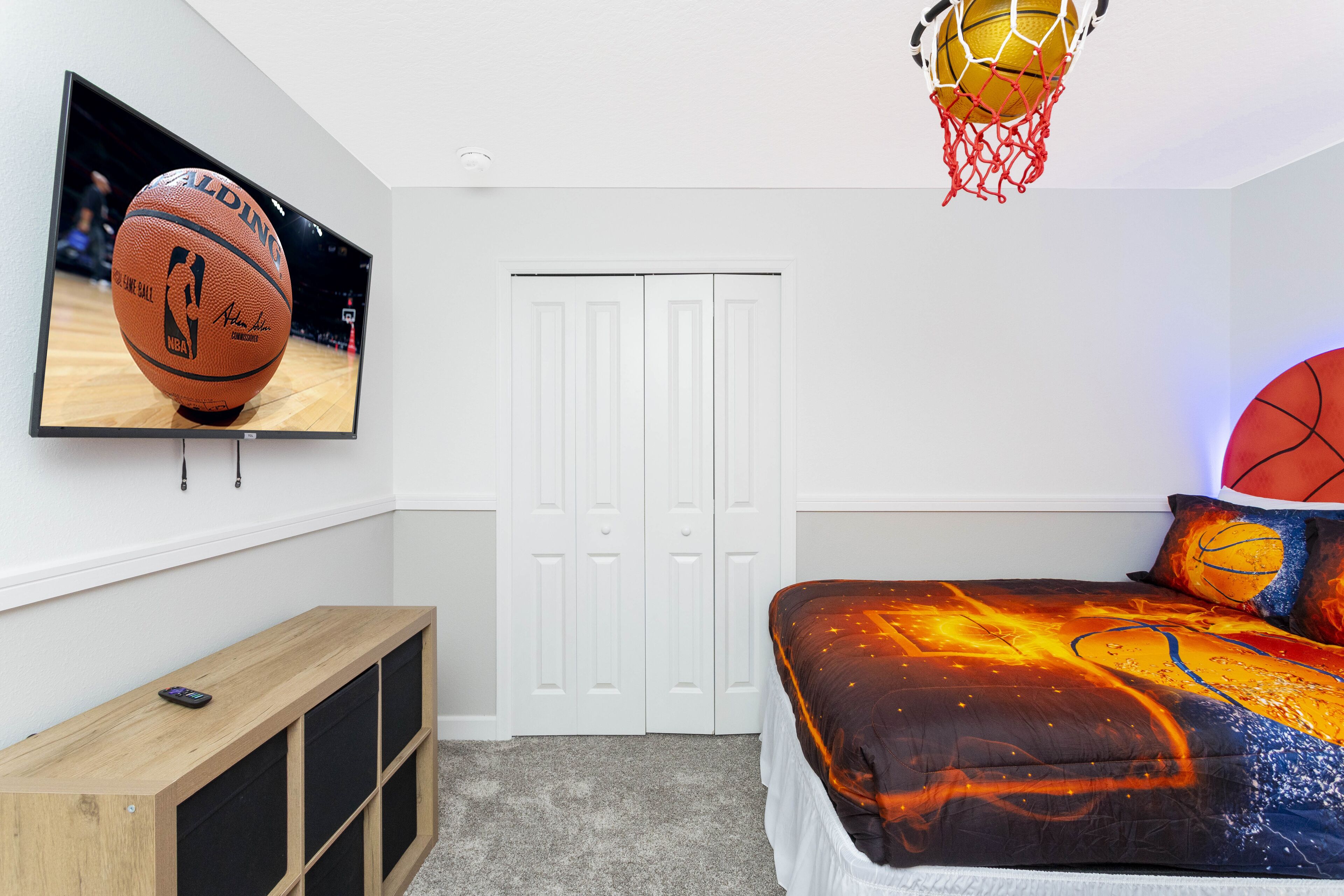 Una camera da letto con un letto, una televisione, un canestro da basket e un armadio in legno.