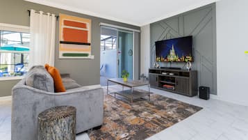 A modern living room with a grey sofa, a coffee table, and a flat-screen TV on a grey wall.