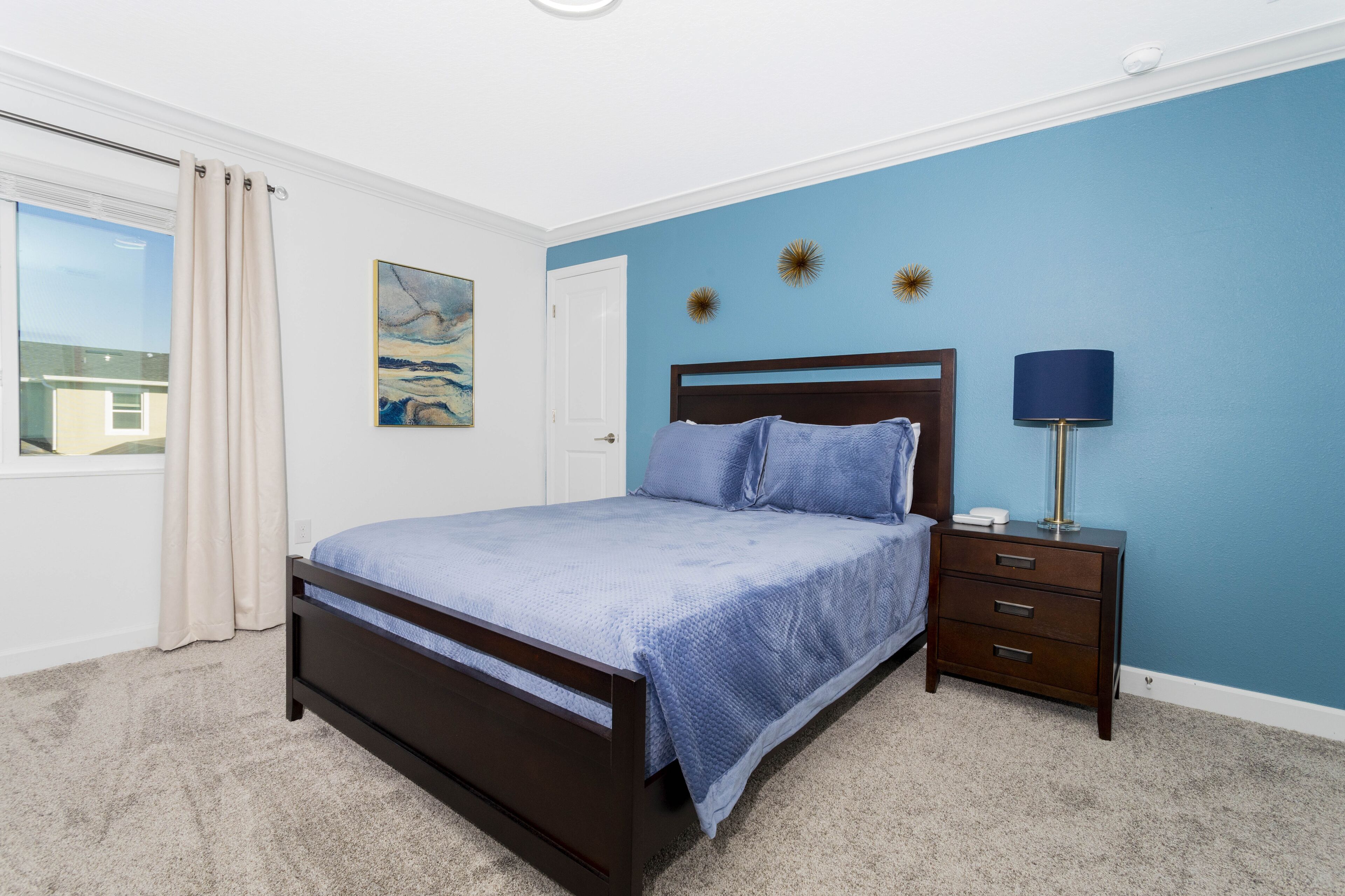 A bedroom with a bed, a nightstand, a lamp, and a painting on the wall.