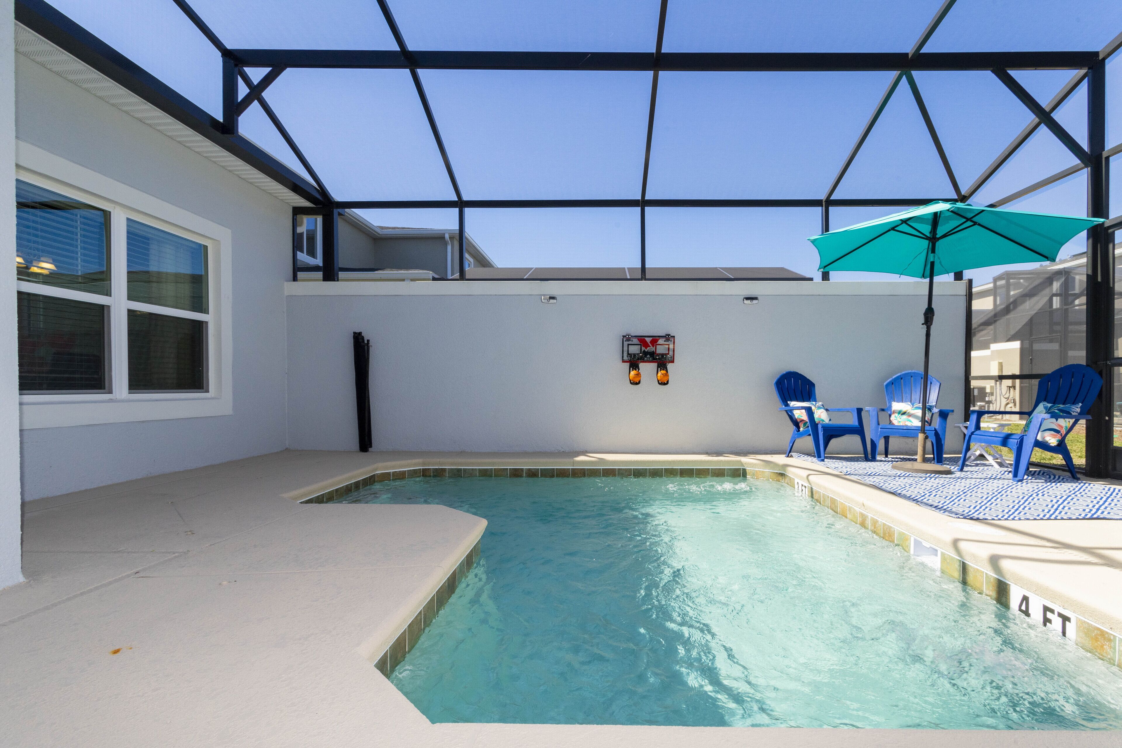 An indoor swimming pool with clear blue water, surrounded by a white pool deck and a glass ceiling.