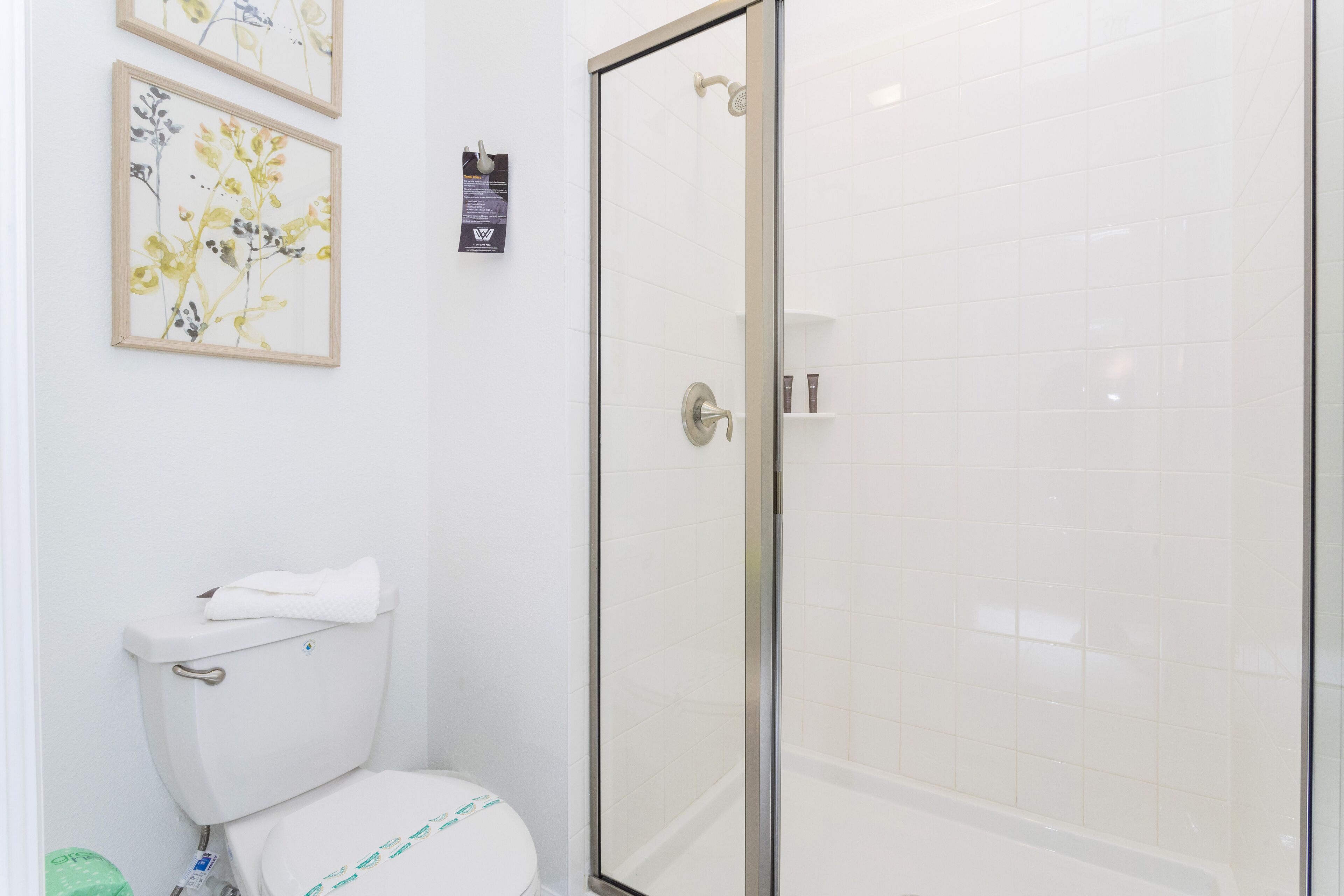 Un baño con inodoro, cabina de ducha de vidrio y dos cuadros de flores en la pared.