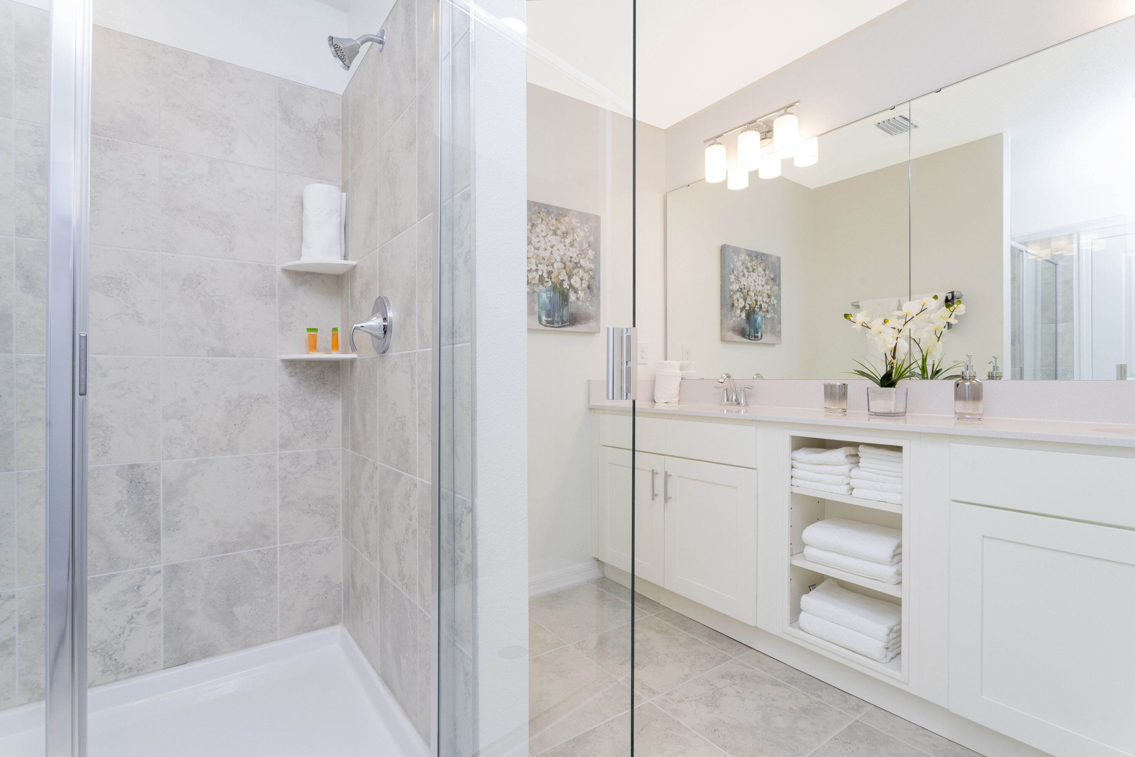 A modern bathroom with a glass shower enclosure, white cabinetry, and a large mirror.