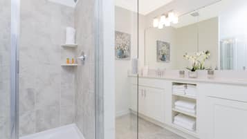 A modern bathroom with a glass shower enclosure, white cabinetry, and a large mirror.
