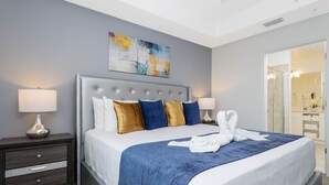 Habitación de hotel moderna con una cama grande, una mesita de noche con cajones, un cuadro colgado en la pared y un baño visible a través de una puerta abierta.