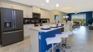 Una cocina moderna con una isla central, electrodomésticos de acero inoxidable y un comedor con taburetes de bar.