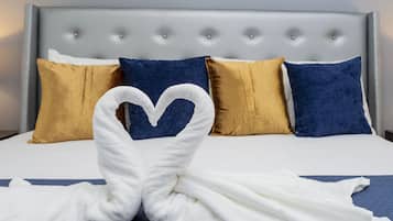 A bed with a tufted headboard, two gold and two blue pillows, and a white towel arranged in a heart shape.