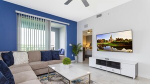 Una sala de estar moderna con un sofá seccional color beige, una mesa de centro blanca y un televisor de pantalla plana montado en la pared.
