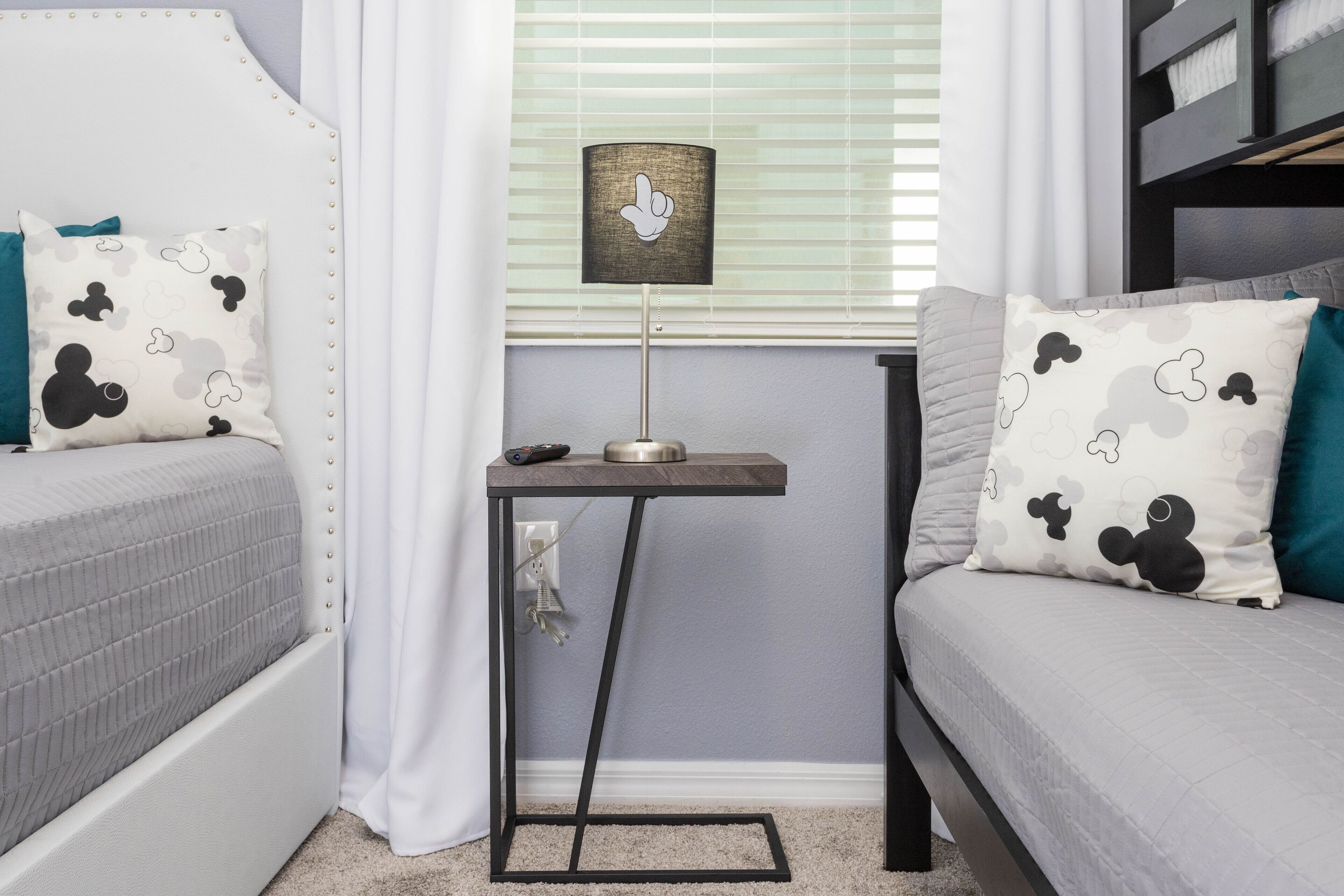 A bedroom with two beds, a bedside table with a lamp, and Mickey Mouse themed pillows.
