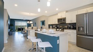 A modern kitchen with white cabinets, stainless steel appliances, and a central island with bar stools.