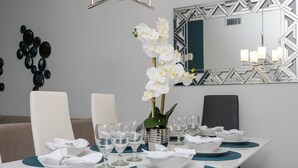 A dining table set with white bowls, plates, and glasses, teal placemats, and a vase with white flowers.