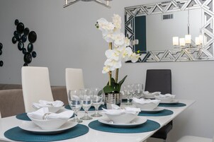 A dining table set with white bowls, plates, and glasses, teal placemats, and a vase with white flowers.