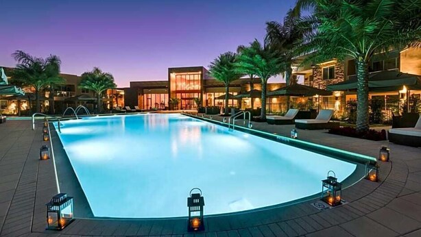 A swimming pool with lounge chairs and palm trees, surrounded by buildings with illuminated windows. - Marvelous 4 Bd Close to Disney @ Magic Village 3153 (Kissimmee)